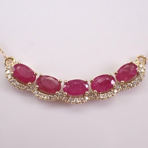 Può includere: Una collana d'oro con cinque rubini ovali rosso intenso. I rubini sono incastonati in un design curvo, impreziosito da piccoli diamanti scintillanti. La collana ha una delicata catena e chiusura in oro.