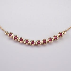 Puede incluir: Un collar de cadena de oro con una fila curva de nueve piedras de rubí rojas.