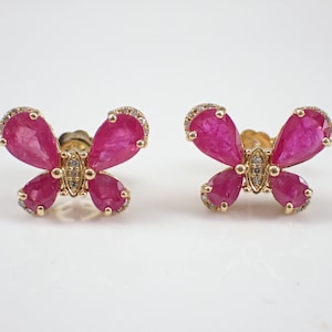 May include: A pair of butterfly stud earrings. Each earring has a gold setting with bright pink gemstones forming the wings and smaller stones along the edges. The centre of each butterfly has a cluster of smaller stones.