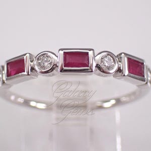 May include: A silver-toned ring featuring an alternating pattern of three rectangular, deep red rubies and four round, clear diamonds. Each gemstone is set in a bezel setting along the band, which displays the text Galaxy Gems in script.