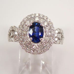 May include: A silver ring featuring a large oval blue sapphire encircled by a double halo of smaller diamonds.