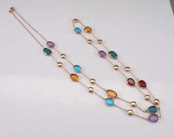 May include: A gold chain necklace with alternating round and oval-shaped gemstones. The gemstones are in shades of blue, purple, orange, and red.