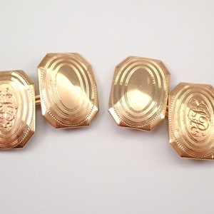 May include: A pair of gold cufflinks with an oval design. One cufflink has an engraved monogram, while the other is plain.