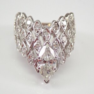 Könnte beinhalten: Ein Ring mit einem birnenförmigen Diamanten und einem filigranen, komplizierten Design. Der Ring ist in Weißgold gefasst und verfügt über eine Reihe kleinerer Diamanten um den Mitteldiamanten.