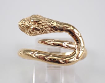 May include: A gold-toned metal ring shaped like a coiled snake. The ring features a detailed, textured head with defined eyes and scales, and a smooth, curved body that wraps around to form an open, adjustable band design with a polished finish.