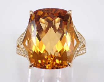 Pode incluir: Um anel marcante com uma grande pedra preciosa facetada amarelo-dourado. O anel apresenta uma citrina de corte retangular almofadado, engastada numa banda de ouro com detalhes de diamantes. O design inclui recortes geométricos e uma haste dividida.