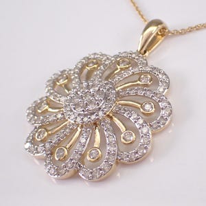 May include: A gold-toned pendant necklace featuring a floral design. The pendant is adorned with numerous small, sparkling diamonds, arranged in a layered pattern. The necklace has a delicate chain.