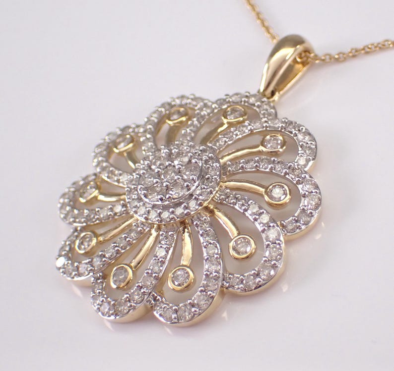 May include: A gold-toned pendant necklace featuring a floral design. The pendant is adorned with numerous small, sparkling diamonds, arranged in a layered pattern. The necklace has a delicate chain.