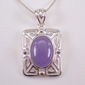 May include: A silver pendant necklace featuring a rectangular frame with a geometric design. The pendant holds an oval, lavender-colored stone. The necklace chain is a delicate silver box chain.