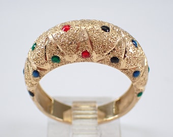 Può includere: Un anello d'oro con una superficie testurizzata e pietre colorate. Le pietre sono rosse, blu, verdi e nere.