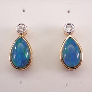May include: A pair of teardrop-shaped earrings featuring polished blue and green opals set in yellow gold bezels. Each earring is topped with a small, round, clear faceted diamond set in a white gold or platinum bezel, creating a two-tone metal design.