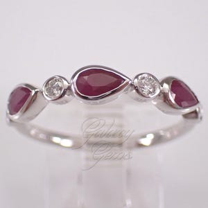 May include: A silver-toned ring featuring a series of alternating pear-shaped deep red rubies and round clear white diamonds set in a bezel style. The band is polished metal, and the text Galaxy Gems is visible in a cursive font across the center.