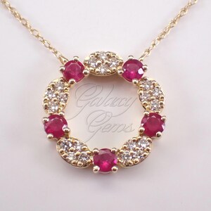 May include: A gold circular pendant necklace featuring alternating round red rubies and clusters of clear white diamonds set in a circular frame. The text Galaxy Gems is visible in the center of the pendant. The pendant hangs from a thin gold chain.