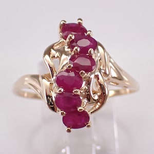 May include: A gold ring with five oval-shaped ruby gemstones set in a swirling design.