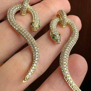 May include: A pair of gold snake earrings with emerald eyes and pave diamond detailing.