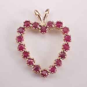 May include: A heart-shaped pendant crafted from gold-toned metal, featuring a series of small, round, deep red rubies set along the entire perimeter. The pendant includes a gold-toned bail at the top for attachment to a chain or necklace.