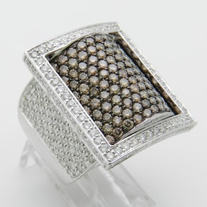 May include: A silver ring with a rectangular face, encrusted with small, round, brown and white gemstones. The ring's band and the frame around the rectangular face are covered in white gemstones, creating a sparkling effect. The ring is set against a light background.