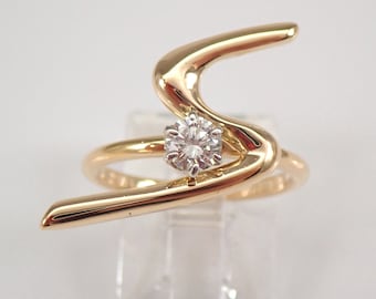 Op de afbeelding: Een gouden ring met een enkele diamant gezet in een gebogen band. De band is gevormd als een gestileerde letter 'S'.