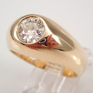 May include: A gold ring with a large, round, clear gemstone set in a raised bezel. The ring has a thick band.