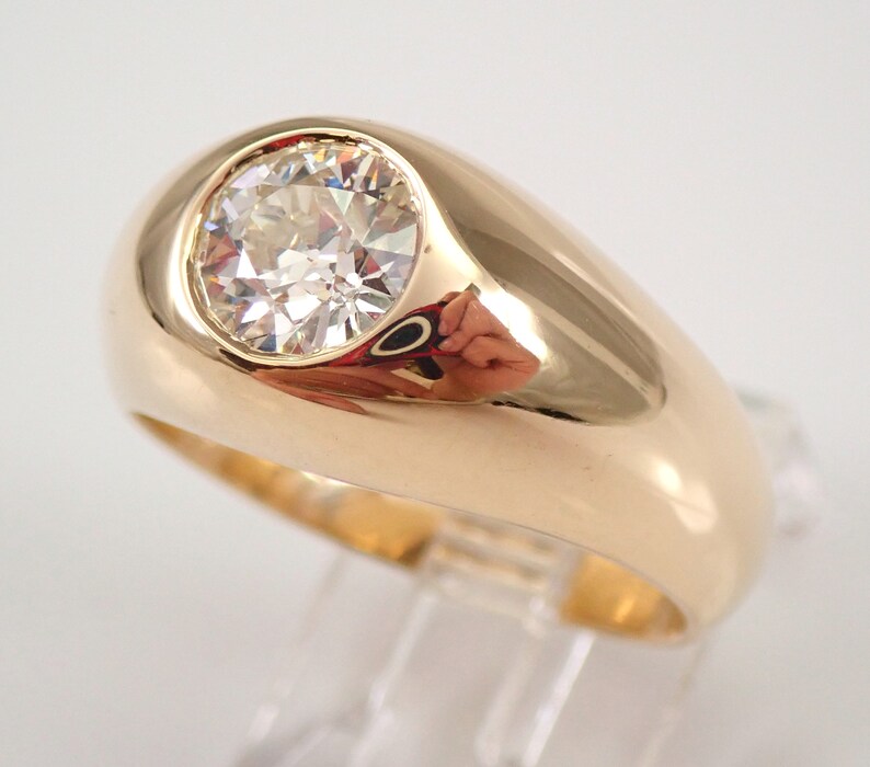 May include: A gold ring with a large, round, clear gemstone set in a raised bezel. The ring has a thick band.