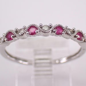 Puede incluir: Un anillo de plata con una serie de piedras rosas y pequeñas piedras transparentes alternadas. El anillo tiene un diseño delicado y ornamentado con un acabado pulido. Las piedras preciosas están engastadas en una fila en la parte superior.