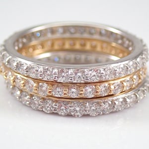 May include: Three diamond eternity bands stacked together. The top band is white gold, the middle band is yellow gold, and the bottom band is white gold.