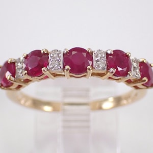 May include: A gold ring with a band set with a series of oval, deep red rubies and small diamonds. The ring's design is classic and elegant, suitable for special occasions. The ring is a beautiful piece of jewellery.