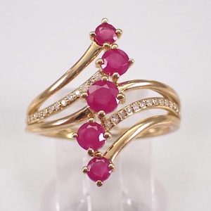 May include: A gold ring with five round, bright red rubies arranged in a flowing design. The ring also features small diamonds set along the bands, creating a luxurious and elegant appearance.