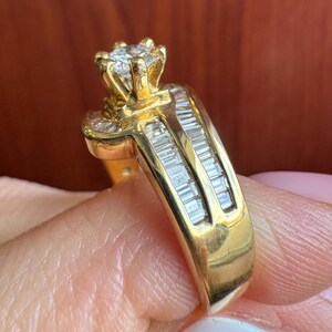 May include: A gold ring featuring a central round brilliant-cut diamond held in a six-prong setting. The band is accented with two parallel rows of channel-set baguette-cut diamonds that extend along the sides of the shank.