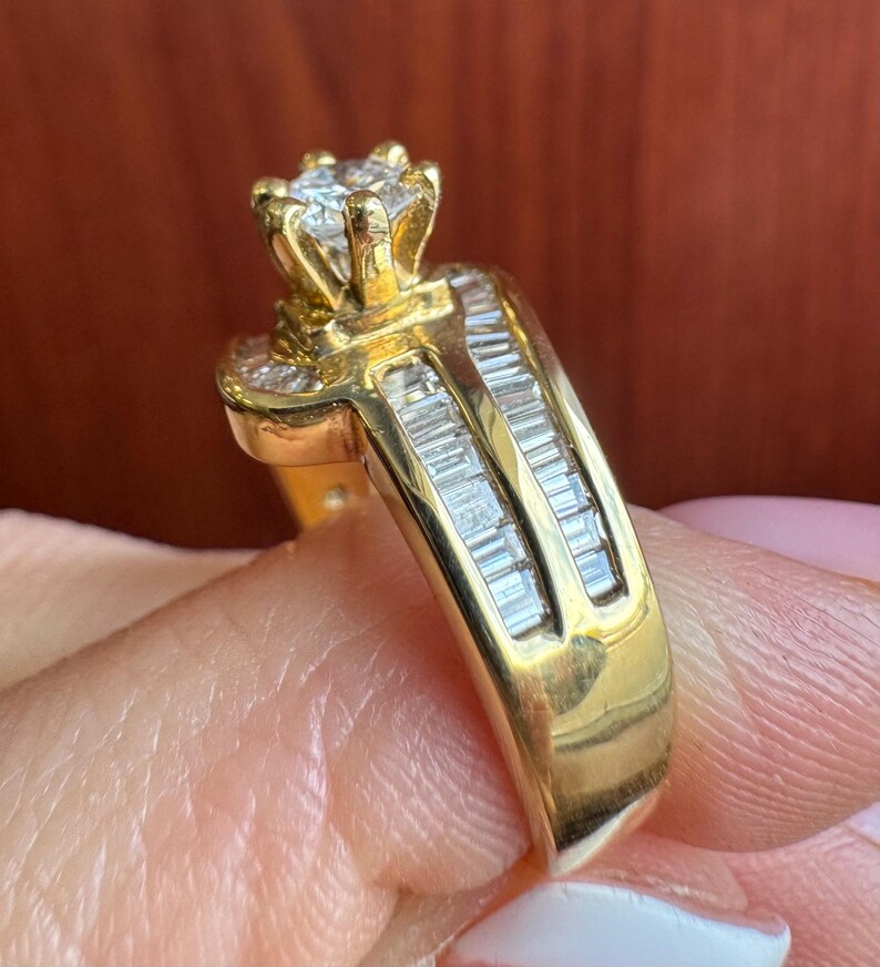 May include: A gold ring featuring a central round brilliant-cut diamond held in a six-prong setting. The band is accented with two parallel rows of channel-set baguette-cut diamonds that extend along the sides of the shank.