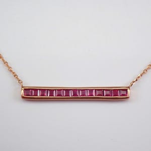 May include: A rose gold necklace with a bar pendant set with red square-shaped gemstones.