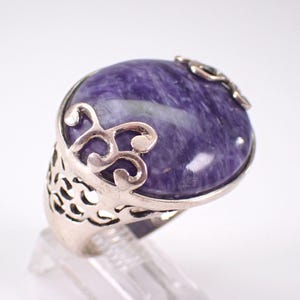 May include: A silver ring with an oval-shaped purple gemstone set in a filigree design.