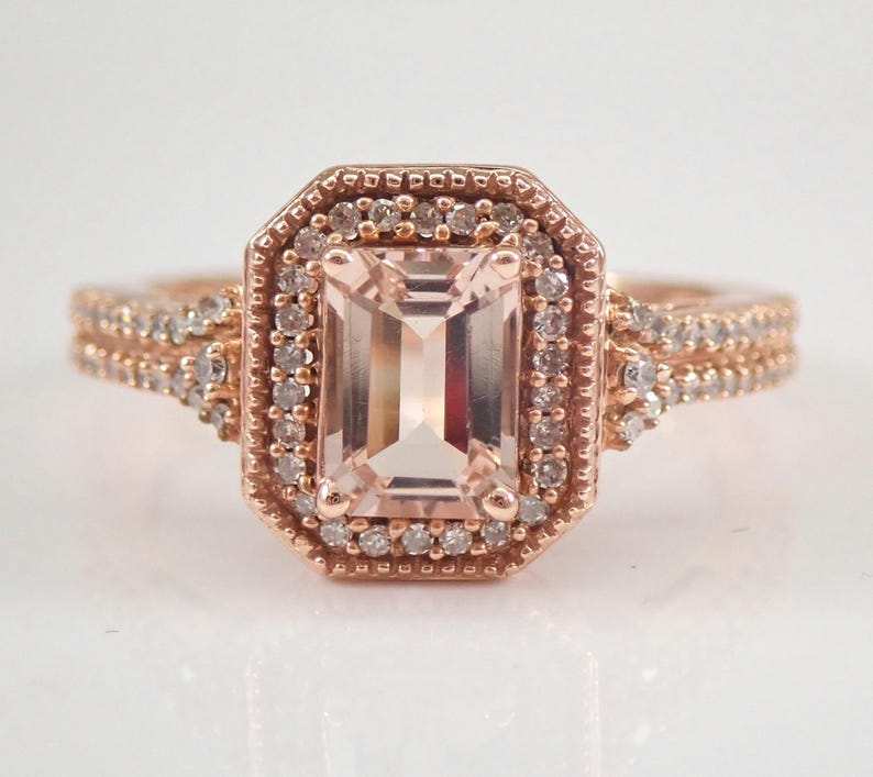 May include: A rose gold engagement ring with a large, rectangular morganite center stone surrounded by a halo of smaller diamonds. The band is also set with diamonds.