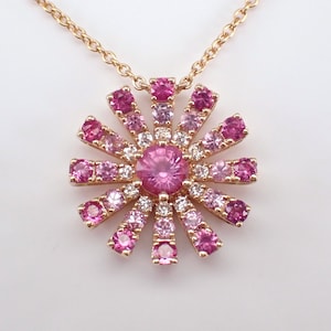 Könnte beinhalten: Eine zarte goldene Halskette mit einem Anhänger aus rosa Saphir. Der Anhänger zeigt einen zentralen rosa Saphir, der von kleineren rosa Saphiren und Diamanten umgeben ist, die in einer blütenartigen Form angeordnet sind.