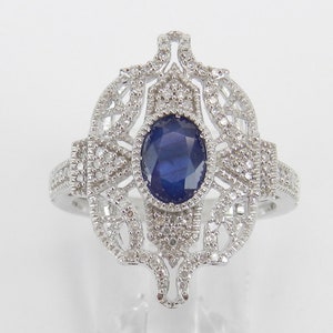 Könnte beinhalten: Ein silberner Ring mit einem blauen Saphir-Edelstein, der von kleinen Diamanten in einem filigranen Design umgeben ist.