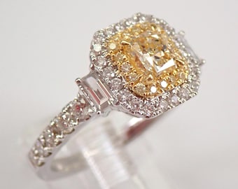 May include: A diamond ring with a large, rectangular, yellow-toned center stone, surrounded by a halo of smaller diamonds. The ring has a double halo design and additional baguette-cut diamonds on the sides. The band is silver-toned and set with small diamonds.