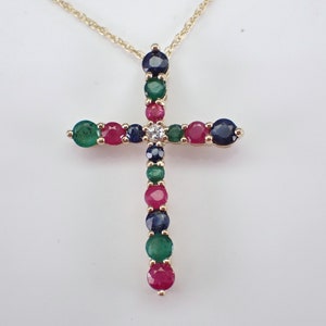 May include: A gold chain necklace with a cross pendant. The cross is adorned with a variety of gemstones, including emeralds, rubies, and sapphires.
