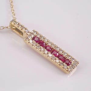 May include: A gold pendant necklace featuring a rectangular pendant. The pendant is adorned with a row of vibrant red gemstones flanked by smaller, clear gemstones. The necklace chain is also gold.