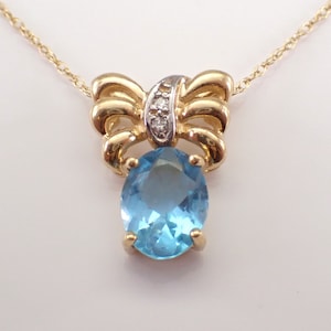 May include: A gold necklace with a blue topaz pendant and a bow-shaped setting with small diamonds.