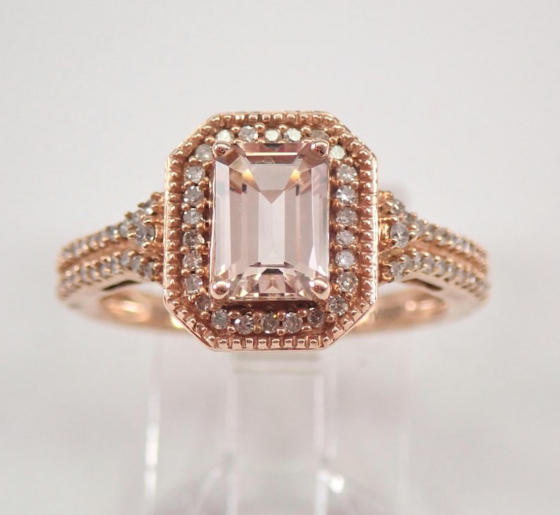 May include: A rose gold engagement ring with a large, rectangular, light pink morganite gemstone surrounded by a halo of smaller diamonds. The band is also set with smaller diamonds.