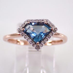May include: A diamond-shaped blue gemstone ring with a rose gold band. The gemstone is surrounded by a halo of small, clear stones. The ring is set against a white background.