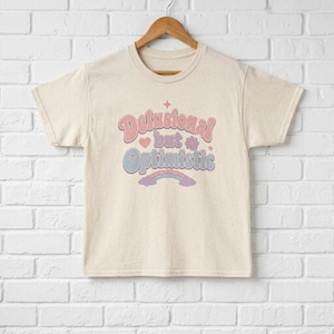 Camiseta "Ilusionista pero optimista" / Texto retro en tonos pastel, corazón y gráfico de arcoíris