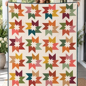 Puede incluir: Una colcha rectangular con un patrón repetitivo de estrellas de ocho puntas en varios colores, incluyendo amarillo mostaza, verde oliva, terracota, rojo oscuro y rosa empolvado, sobre un fondo crema con un borde azul verdoso oscuro.