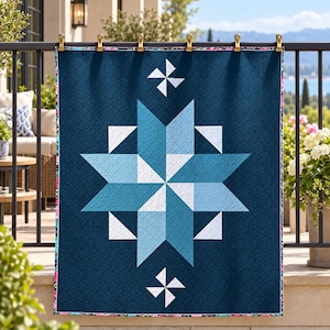 May include: A rectangular quilt featuring a dark navy blue background with a central eight-pointed star pattern in shades of light blue, teal, and white. The quilt includes small white pinwheel accents above and below the star and a floral border.