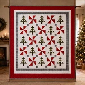Op de afbeelding: Een rechthoekige quilt met een herhalend patroon van groene dennenbomen en rode windmolenblokken op een witte achtergrond. De quilt is omlijst door een zwart-wit geblokte rand en een brede, effen rode buitenrand met stikseldetails.