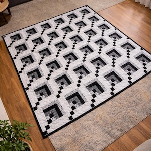 May include: A black and white geometric quilt with a repeating square pattern. The quilt features a white background with black and gray squares arranged in a grid. The quilt is placed on a light-colored rug and hardwood floor.