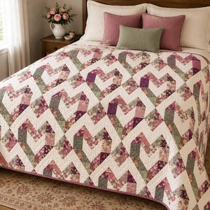 May include: A bed quilt featuring a repeating heart pattern constructed from patchwork fabric squares in shades of mauve, sage green, and cream. The quilt is draped over a bed with two large cream pillows, two mauve square pillows, and one sage green lumbar pillow.