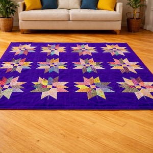 May include: A large, rectangular quilt with a deep purple background. The quilt features a repeating pattern of colourful starburst designs. The stars are made of various patterned fabrics in shades of red, yellow, blue, and green.