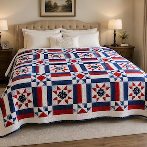 Op de afbeelding: Een quilt met een herhalend geometrisch patroon in rood, wit en blauw. Het ontwerp bevat stermotieven met witte centra en blauwe achtergronden, afgewisseld met effen rode en blauwe rechthoekige blokken en witte rasterranden.