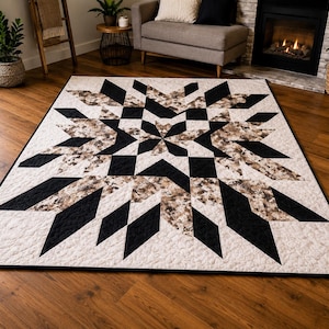 May include: A large, geometric quilt with a starburst design. The quilt features black, tan, and cream-colored diamond and triangular shapes. The quilt is placed on a hardwood floor in a living room setting.